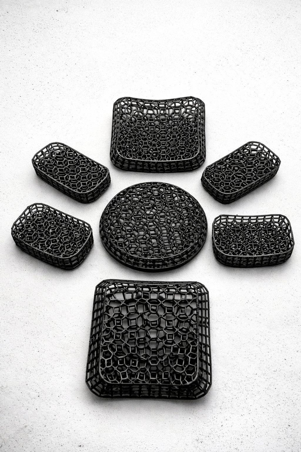 Collection of seven black woven plastic baskets in various rectangular and round shapes arranged on a white surface